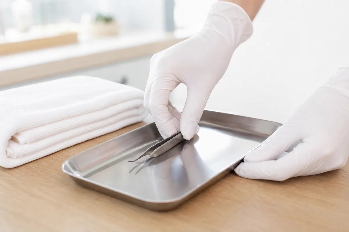 Mains gantées d’une praticienne préparant un plateau d’instruments stériles en institut